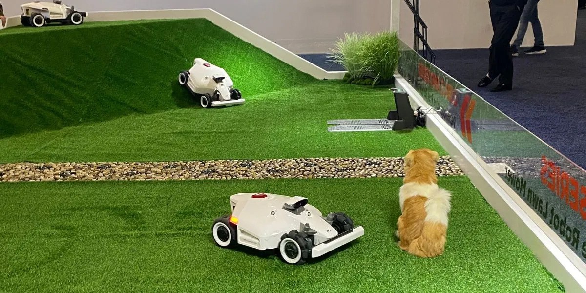 Three white robot lawn mowers on green turf hill