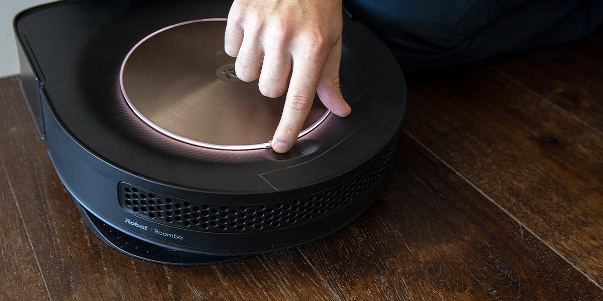 Person pushing button on top of Roomba