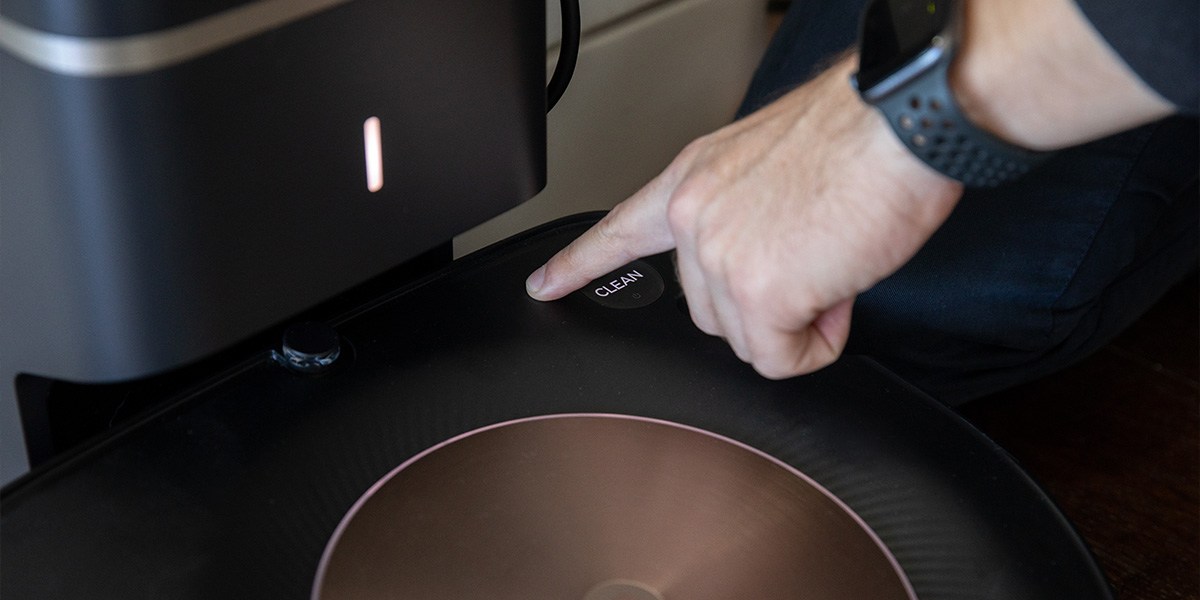 Finger touching "Clean" button on robotic vacuum