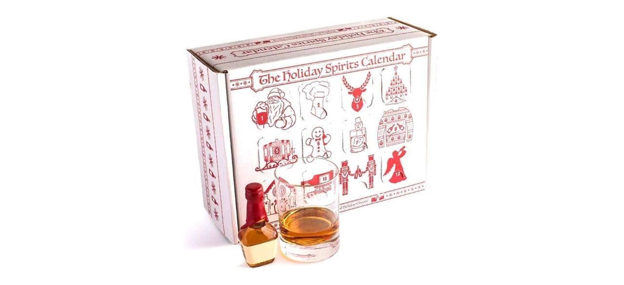 white advent calendar box with red Christmas designs next to a glass of some alcoholic beverage