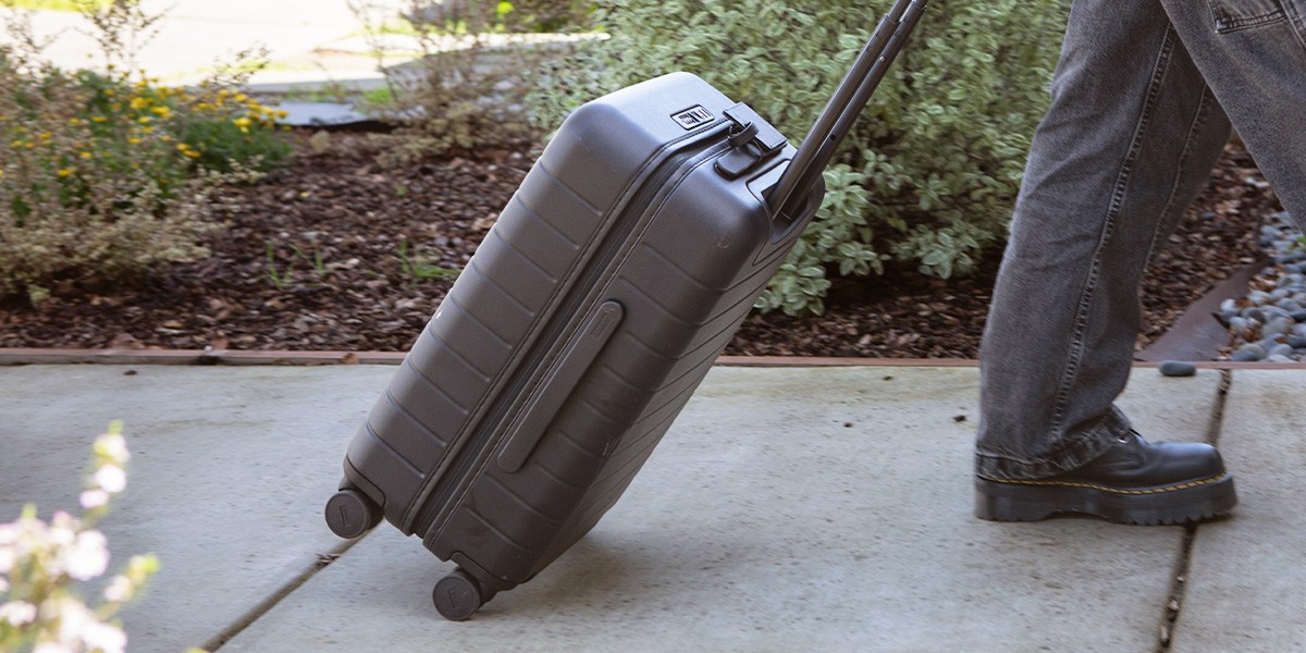 Person pulling carry-on bag on sidewalk