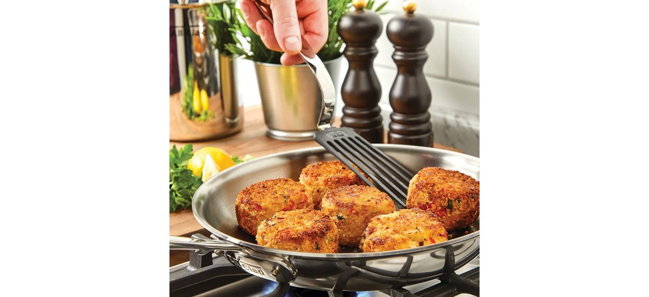 Person cooking with All-Clad D5 Stainless Polished Deep Skillet on stovetop