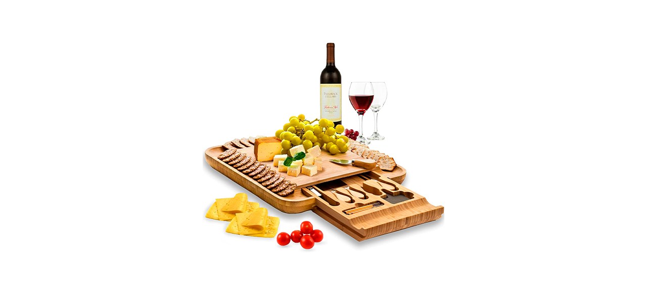 A wooden charcuterie board that has one slide-out portion to hold spreading tools/knives