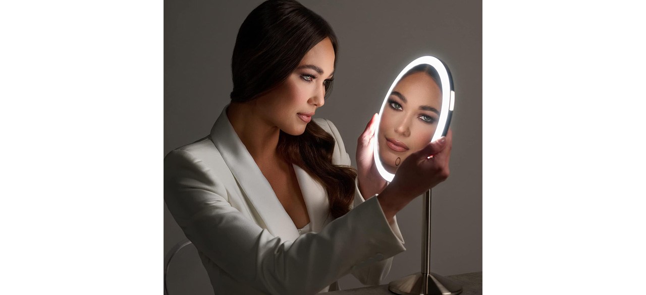 woman looking into Ilios Lighting Cordless Bright LED Makeup Mirror in a dark room