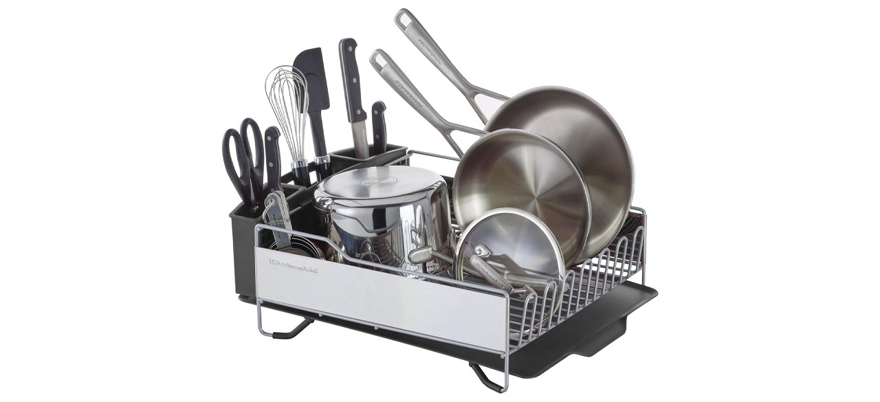 A full-size dish rack with dishes stored in it. It has a spot on the side to hold smaller utensils.