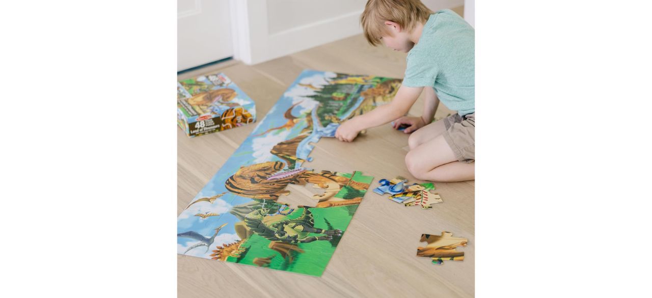 Child putting together large dinosaur puzzle on hardwood floor