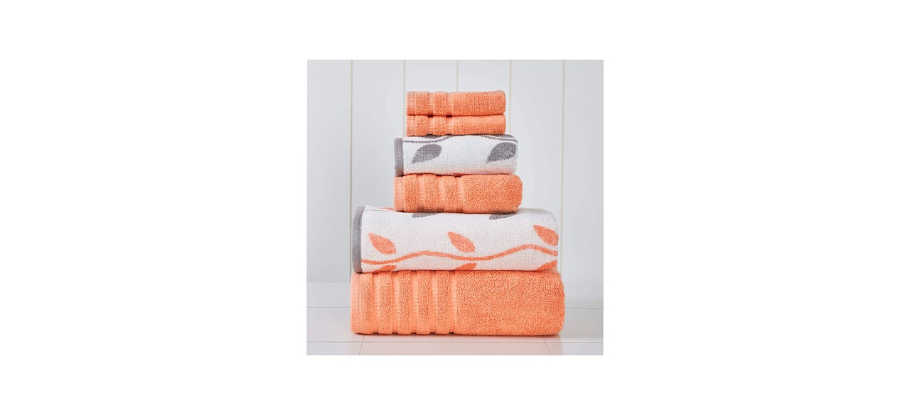 6 towels folded on top of each other. 4 are orange and two are white with leaf designs on them (one with orange leaves and one with gray leaves)