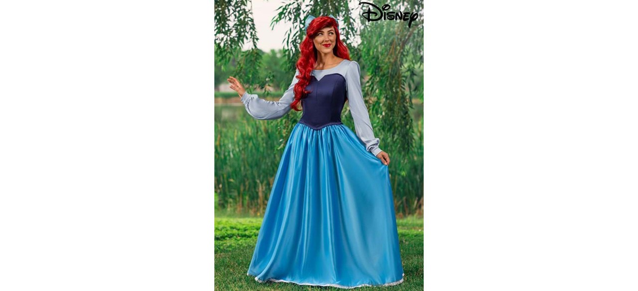 A woman wearing a Little Mermaid costume dress and standing in a field with trees