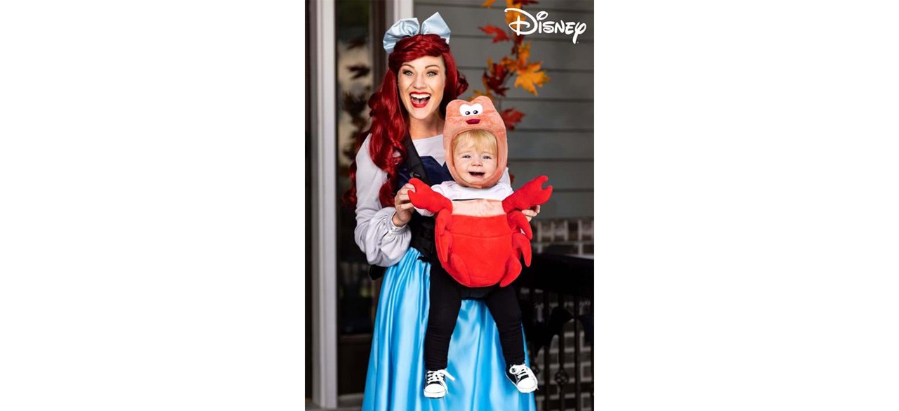 A woman holding a baby in a Disney Sebastion baby carrier costume cover