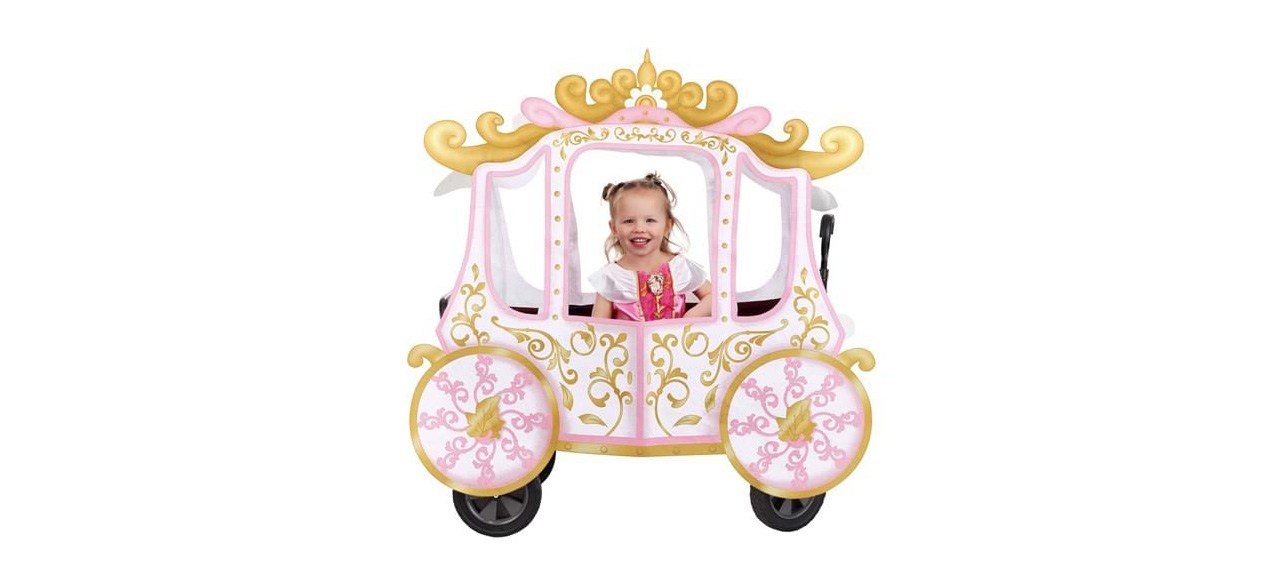 A young girl dressed in a princess costume looking out of a wagon decked in a princess carriage cover accessory