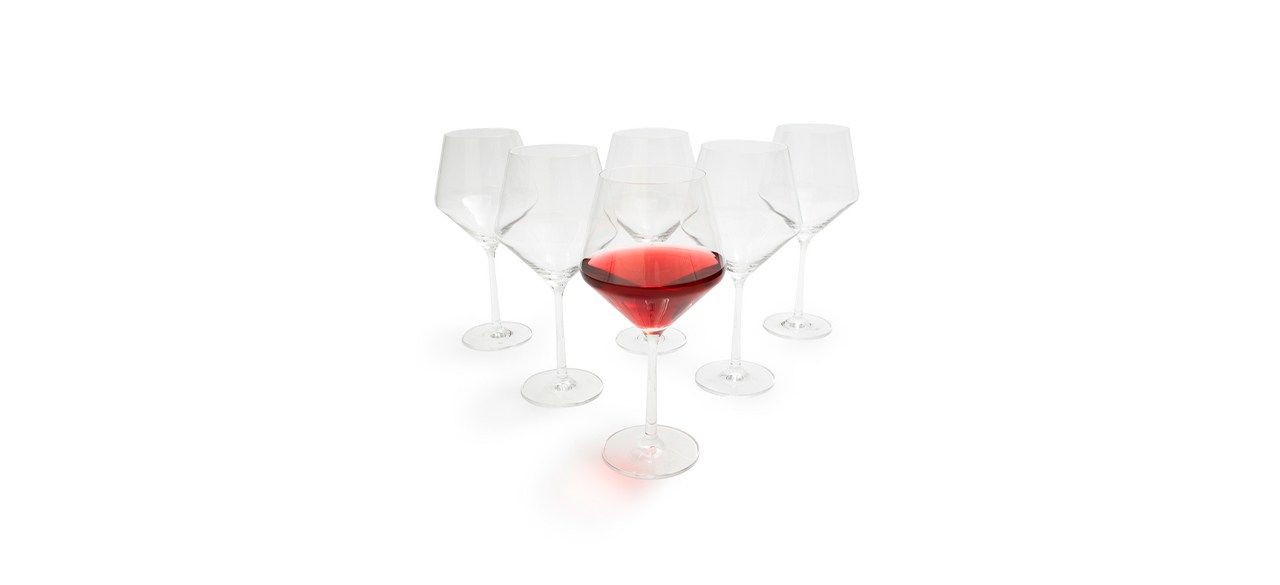 Six wine glasses arranged in a triangle, with the one in front being filled with red wine