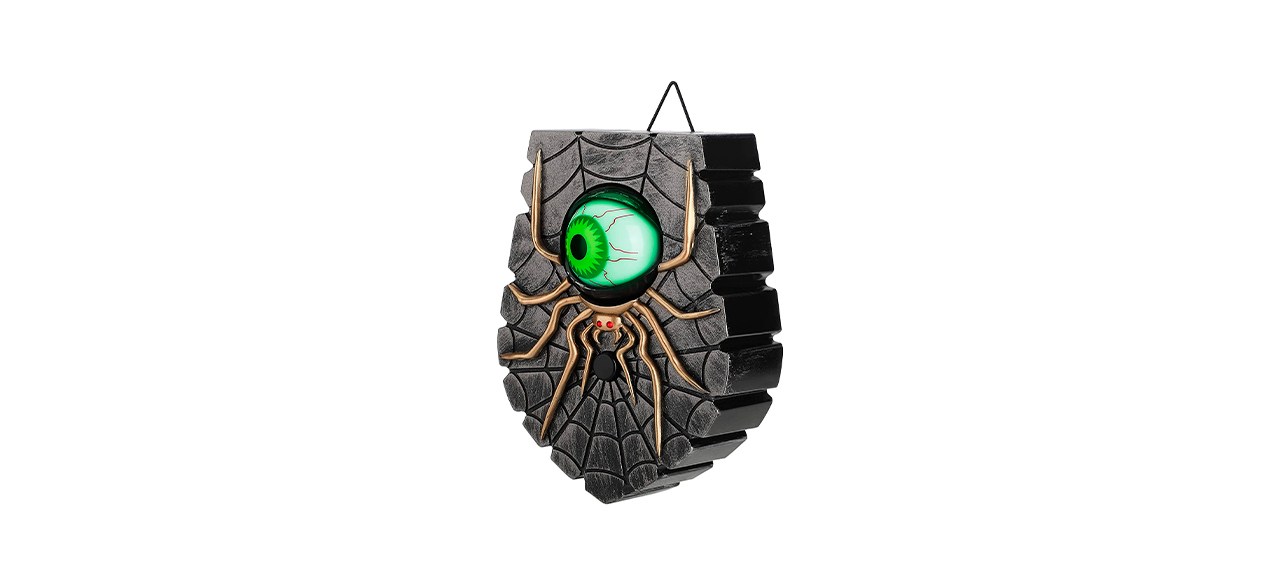 A doorbell that looks like it's made of stone with a cobweb, a spider and a green luminescent eyeball on it.