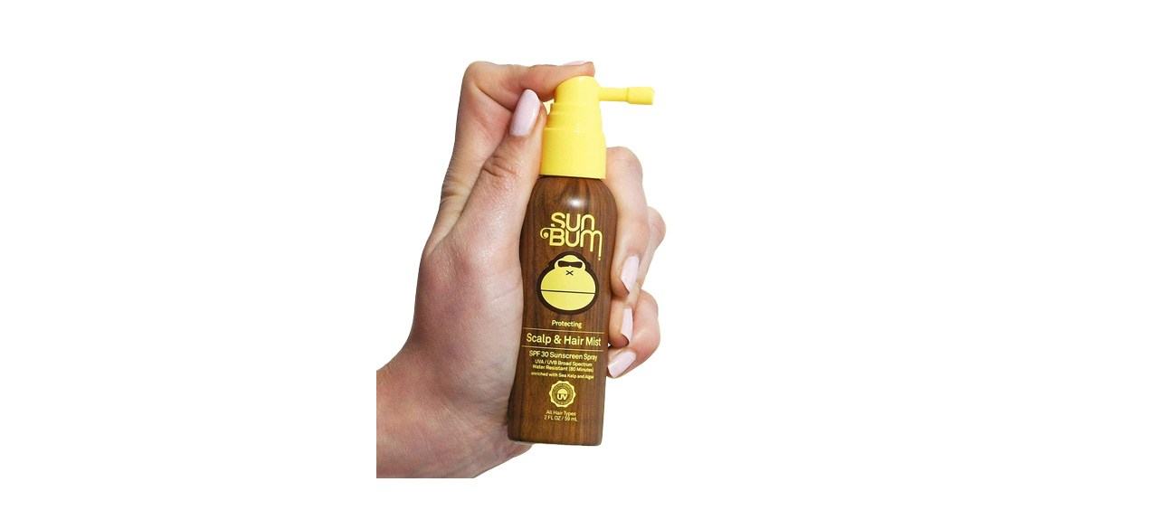 Hand holding Sun Bum Original SPF 30 Sunscreen Scalp and Hair Mist on white background 