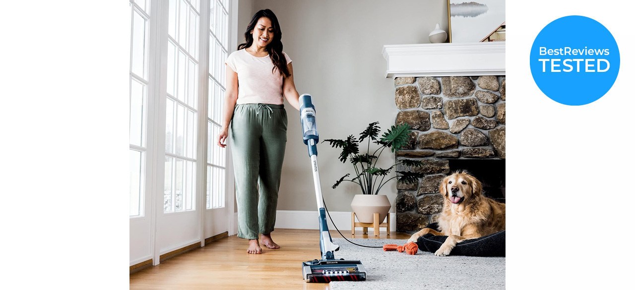 Woman using Shark HZ3002 Stratos Ultralight Corded Stick Vacuum on hard flooring and carpet with dog sitting nearby