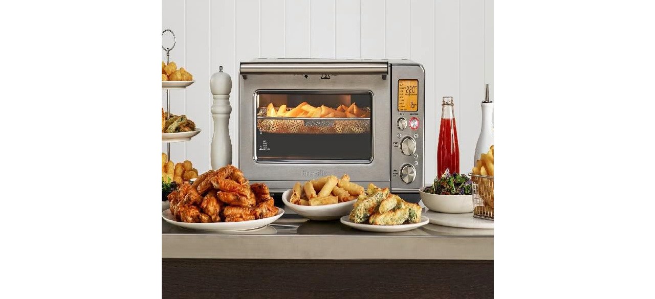 Breville Smart Oven Air Fryer on countertop with plates of fries and chicken wings in front