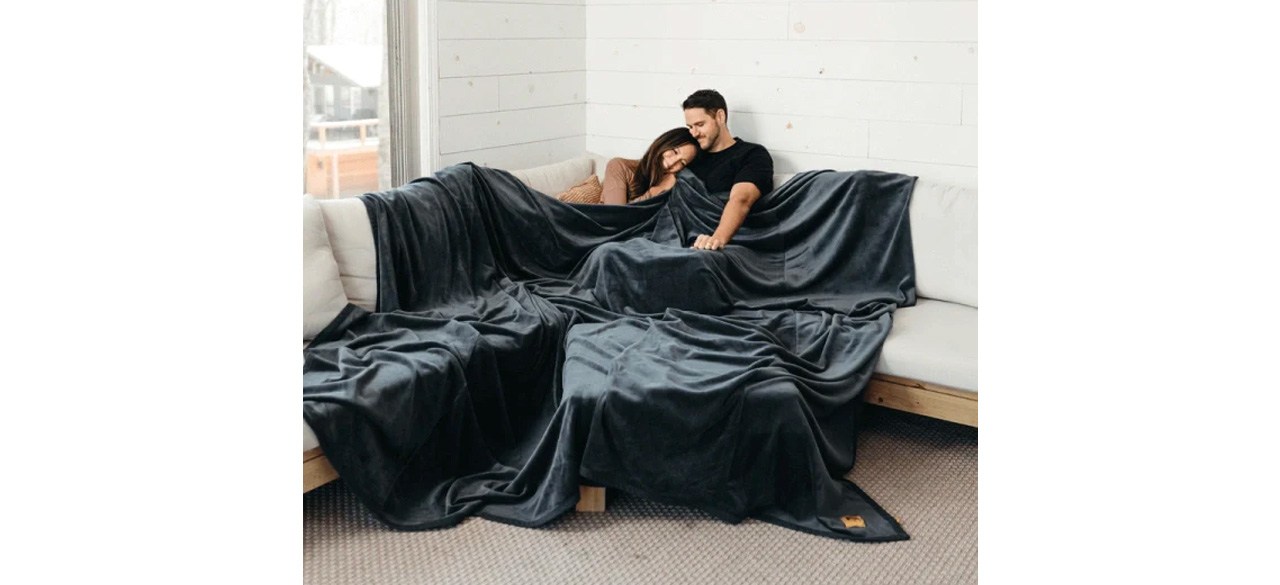 Couple on sofa with black Big Blanket Co Original Stretch Blanket