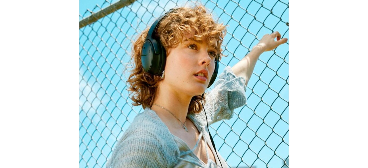 Woman with hand on fence listening to Bose QuietComfort Wireless Noise Cancelling Over-the-Ear Headphones