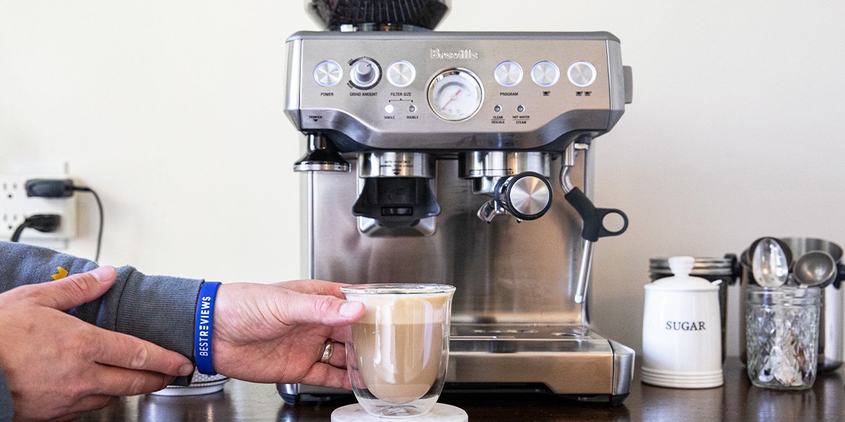 Hand holding cup of espresso in front of Breville Barista Barista Express Impress