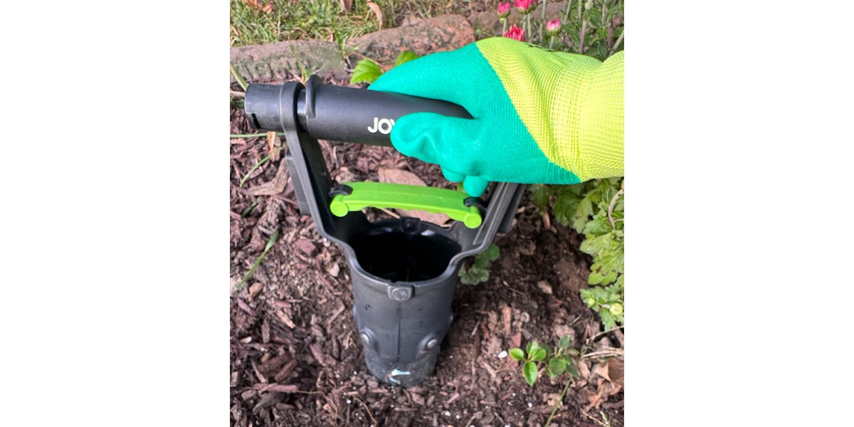 Bulb tool being pushed into soil by hand in garden glove.