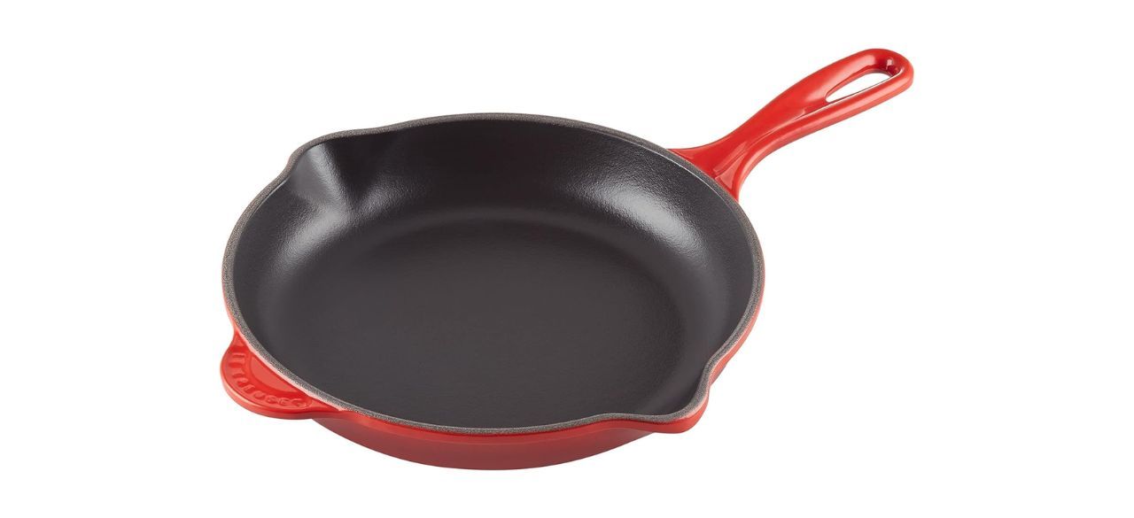 A cast-iron skillet with an enameled orange bottom and a traditional black interior