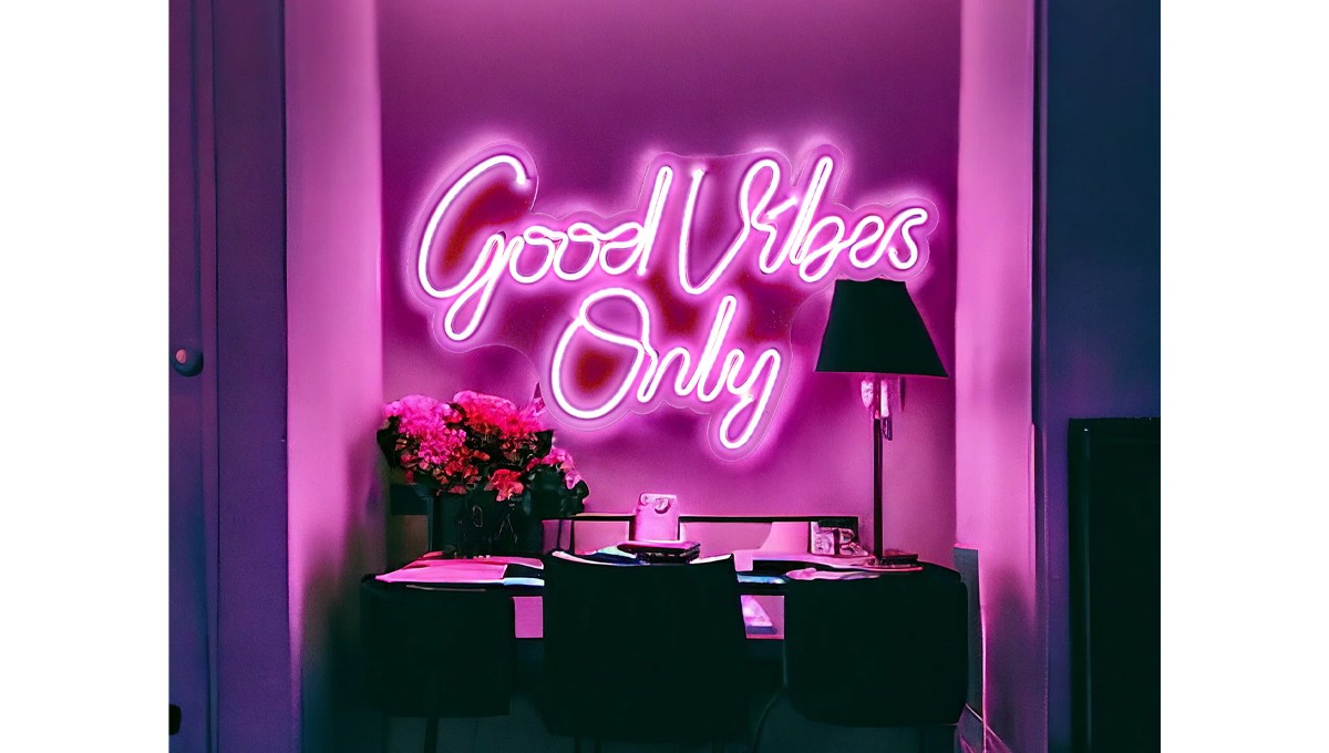 A pink "Good Vibes Only" neon sign on a wall above a desk in a dark room.