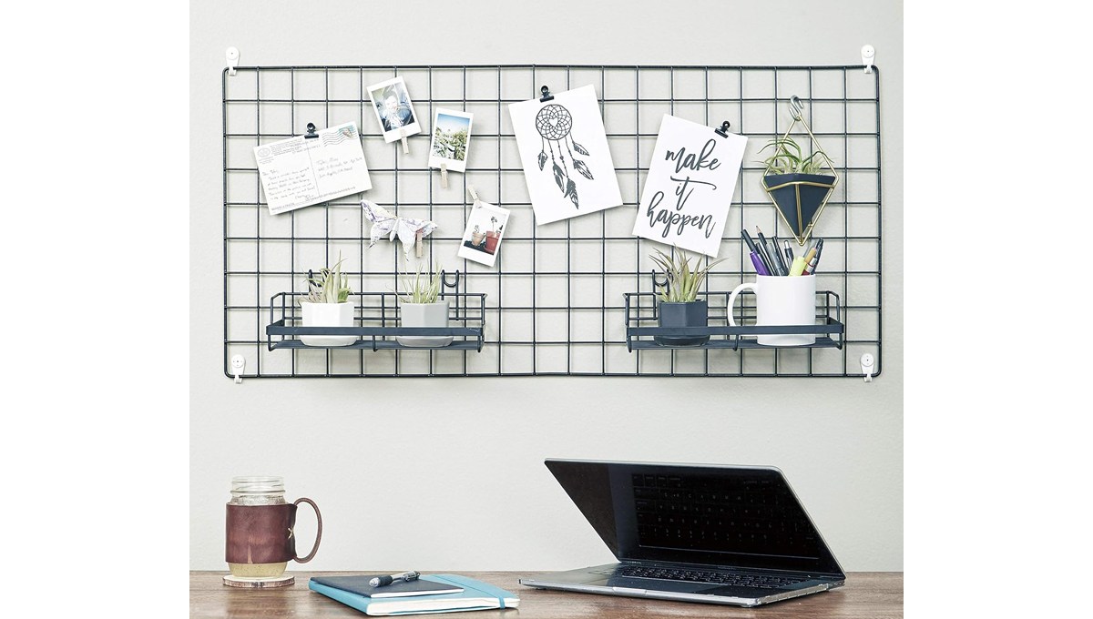 The TRUSTODY Wire Hanging Wall Grid hanging on a wall behind a desk with a drinking glass, book and laptop on it.