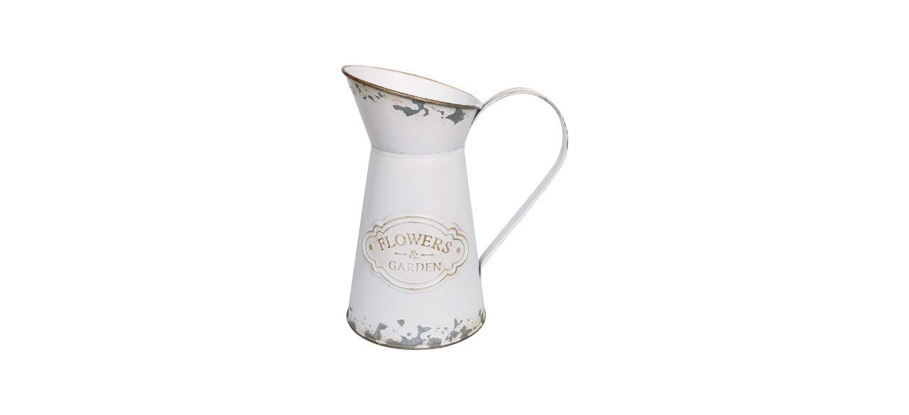 A distressed, metal vase, painted white, shaped like a milk jug with a handle. Text on it reads: Flowers & Garden.