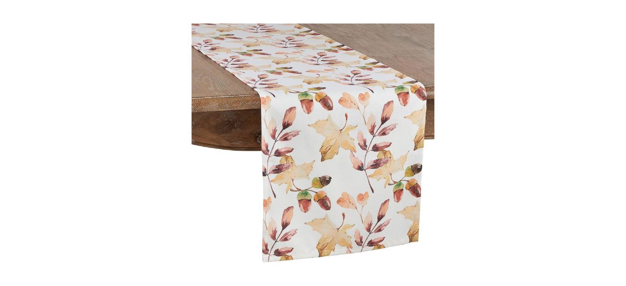 A white table runner with printed designs of brown leaves and acorns