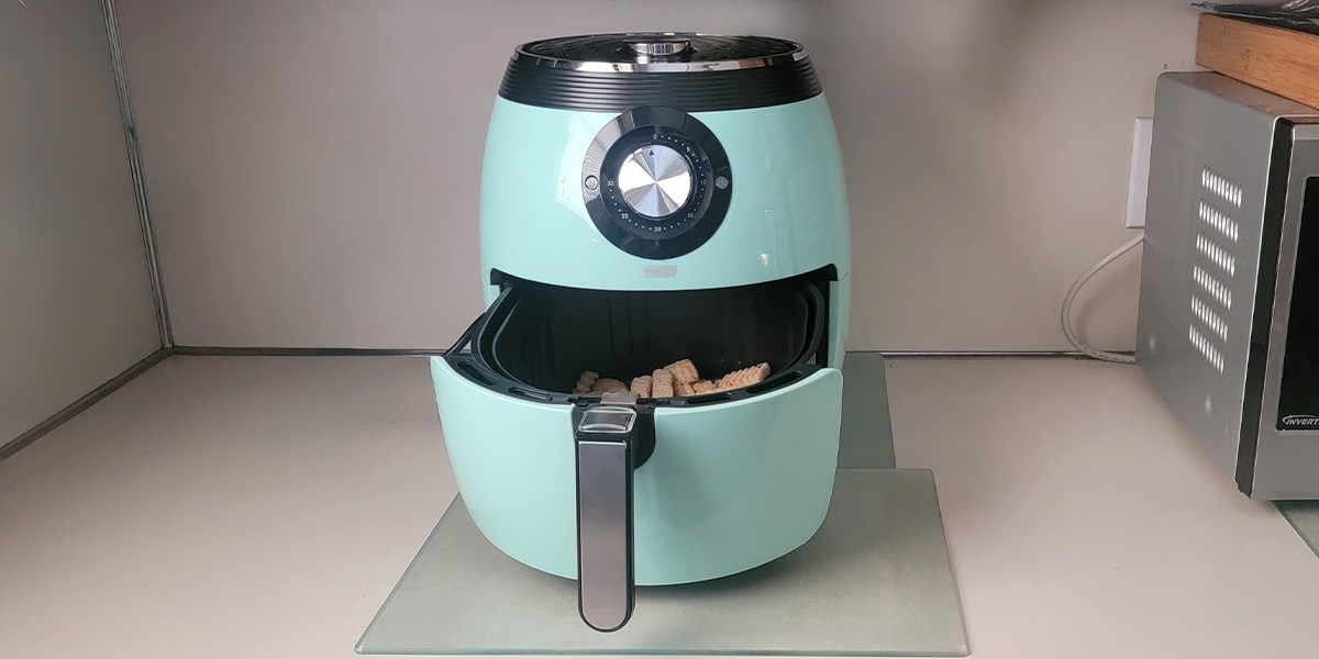 Teal air fryer on kitchen counter with basket open