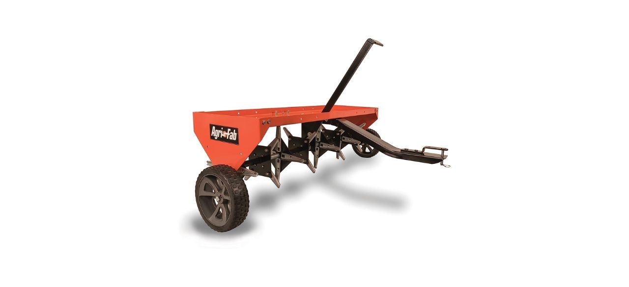 An orange tow-behind lawn aerator with several attached spikes and two wheels