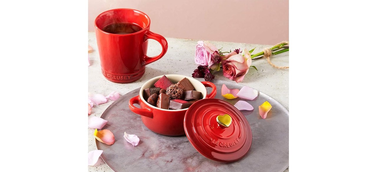 Red Le Creuset Cerise with Gold Heart Knob Stoneware Mini Round Cocotte nex to red coffee cup