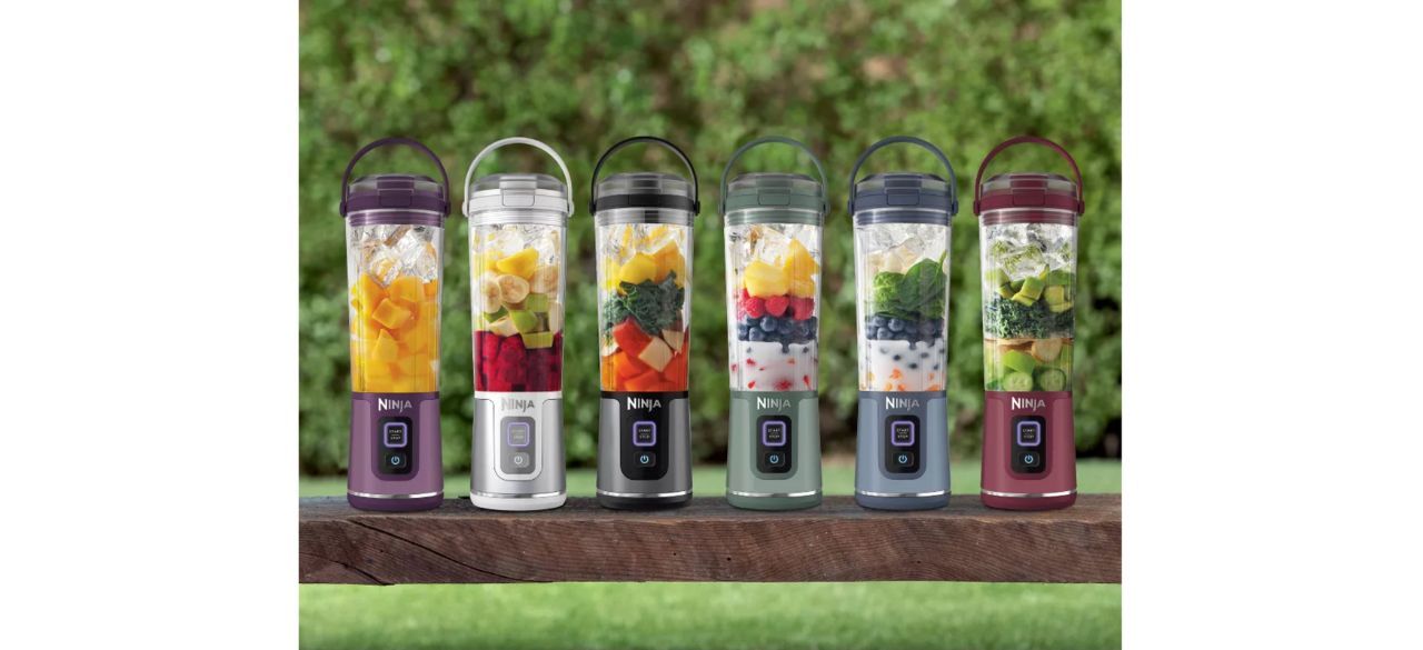 Six Ninja blast portable blenders in different colors on a bench with a grassy background